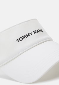 White cotton cap with a curved visor. Features a prominent black "TOMMY JEANS" logo on the front panel, accentuated by clean stitching.