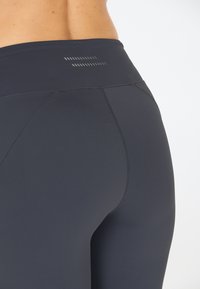 Leggings neri a vita alta realizzati in tessuto elasticizzato, caratterizzati da una texture liscia e cuciture a contrasto lungo le giunture.