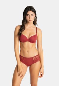Ensemble de lingerie comprenant un soutien-gorge avec des bordures en dentelle rouge et un string assorti. Texture de tissu lisse avec des bretelles réglables et des accents de dentelle détaillés sur les côtés.