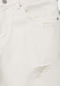 Jean en denim blanc avec poches avant et deux zones usées et effilochées près du haut et du milieu du tissu.