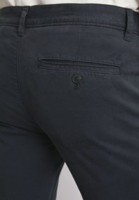 Marineblaue Hose aus glattem Stoff, mit einer Gesäßtasche mit Knopfverschluss und einem schlanken Schnitt. Dezente Markenkennzeichnung auf dem Stoff.
