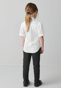 Vit kortärmad skjorta, mörkgråbyxor, blanka svarta skor och ett blårutigt hårband synligt bakifrån. Enkelt och funktionellt design.