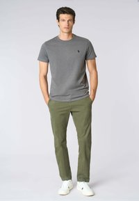 T-shirt grigia in cotone con un piccolo logo, abbinata a chinos verde oliva e sneakers bianche. Design semplice, vestibilità regolare e texture liscia.