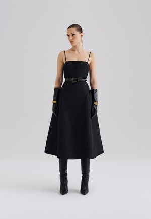 Svart midi-kjole med tettsittende bodice, tynne stropper og belted midje. Inkluderer elegante hansker og spisse hæler. Glatt tekstur.
