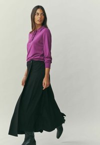 Fuchsia long-sleeve top with ruffled collar, paired with a black floor-length skirt. Black ankle boots complete the outfit.
