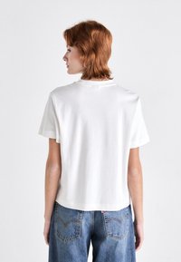 Weißes Baumwoll-T-Shirt mit entspannter Passform, kurzen Ärmeln und Rundhalsausschnitt, kombiniert mit blauen Jeans aus Denim, die Taschen und Nähdetails aufweisen.