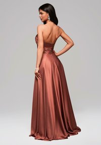 Abito aderente senza spalline in satin ruggine, con corpino arricciato e gonna fluida con morbide pieghe, accentuato dalla chiusura con zip sul retro.