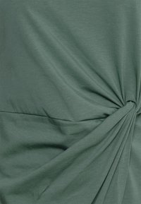 Zelený, lehký, elastický top s uzlovým detailem v pase a hladkou texturou, s jemným žebrováním po celé látce.