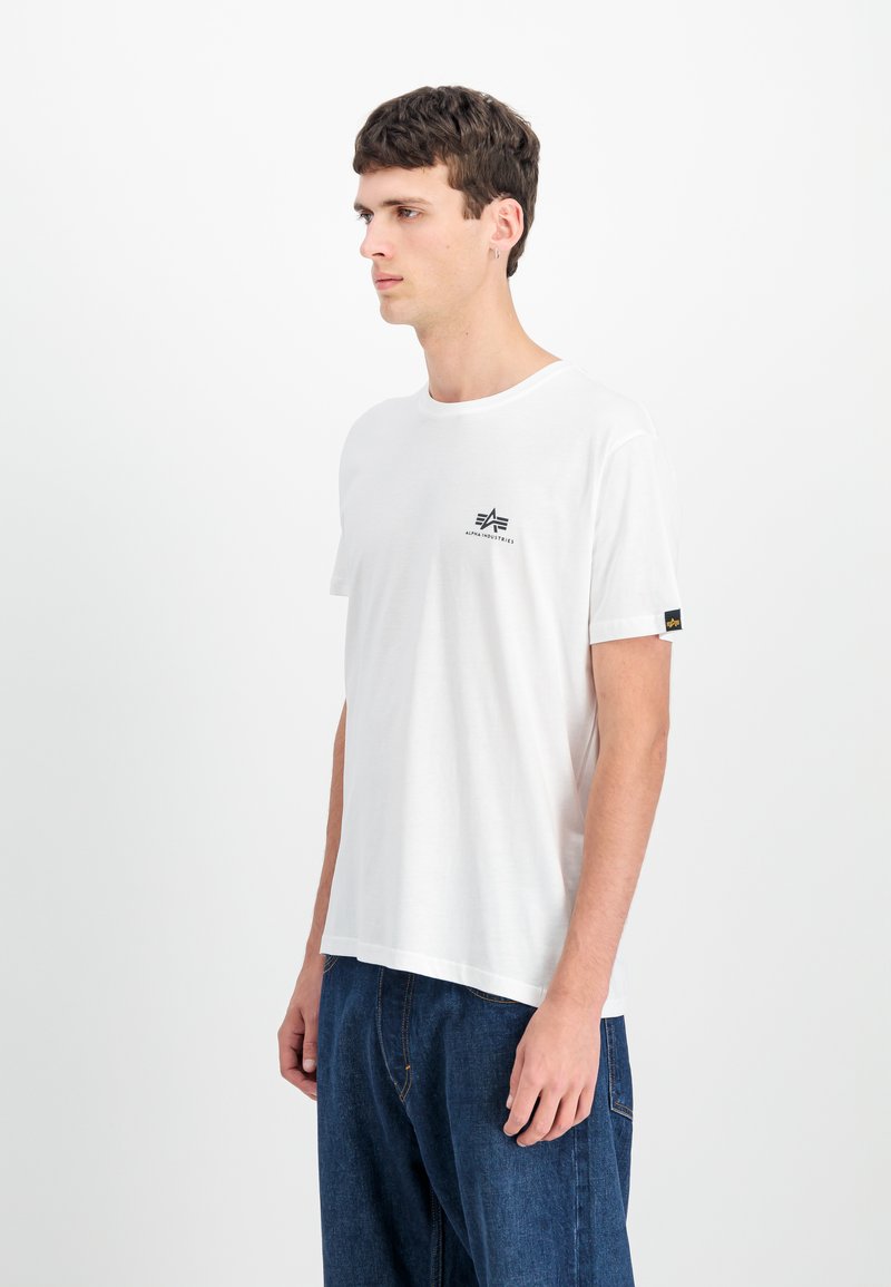 Balta kokvilnas t-krekls ar īsām piedurknēm, apaļu kakla izgriezumu un mazu melnu logo uz krūtīm. Saskaņots ar ziliem džinsu biksēm.