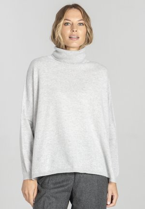 Jasnoszary sweter typu golf wykonanego z miękkiego materiału, o luźnym kroju, z opadającymi ramionami i ściągaczami na dolnym brzegu. Połączony z szarymi spodniami.