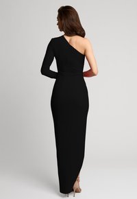 Czarna suknia z jednym długim rękawem i odkrytym ramieniem. Materiał jest gładki i dopasowany, z wysokim rozcięciem z tyłu.