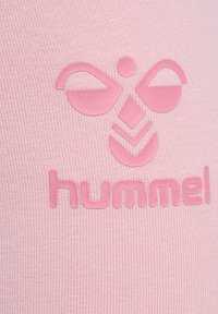 Textile rose clair avec une texture côtelée, featuring a logo surélevé en forme d'abeille stylisée aux éléments stylisés et le mot "hummel."