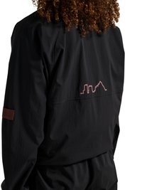 Curly-haired person wearing a black jacket with a minimalist pink city skyline design on the upper back and a brown patch on the sleeve.