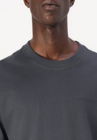 Sweatshirt din bumbac gri închis, cu guler rotund ribbed și branding subtil pe piept. Textură netedă, design casual.