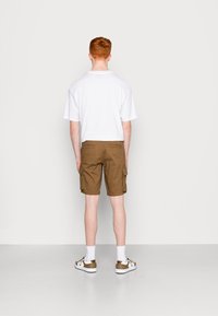 T-shirt blanc à manches courtes, shorts cargos marron avec poches latérales, chaussettes blanches et baskets avec des accents marron, vus de dos.