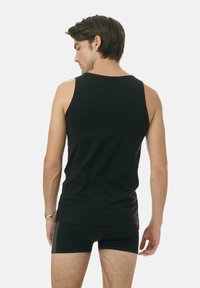 Czarny top na ramiączkach wykonany z miękkiej bawełny, o prostym designie bez wzorów. Tył ma zaokrąglony dekolt i szerokie otwory na ramiona.