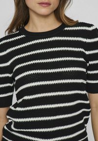 Suéter de manga corta a rayas en blanco y negro con un patrón de punto texturizado y un cuello de canalé.