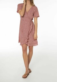 Kortärmad omslagsklänning i röd med blommönster, tillverkad av lättviktsmaterial. Har resår i midjan och volangkant.