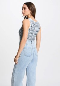 Haut sans manches rayé bleu et blanc avec un col rond, associé à un jean en denim bleu clair taille haute et des bracelets en superposition.