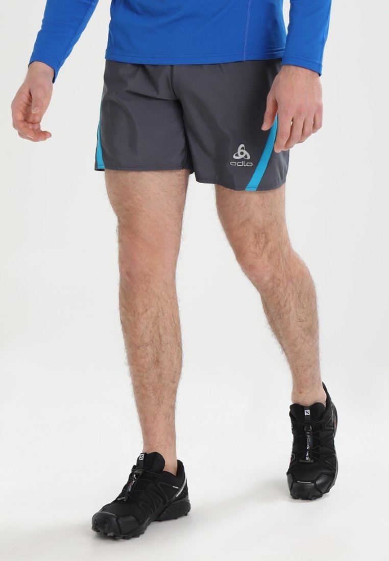 Pantalones cortos deportivos grises con acentos turquesa, hechos de un tejido ligero; combinados con unas zapatillas de correr negras y una camiseta de manga larga azul.
