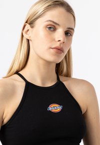 Svart halterneck-top i bomull med en färgglad "Dickies"-logotyp på bröstet. Slät textur med tunna band.