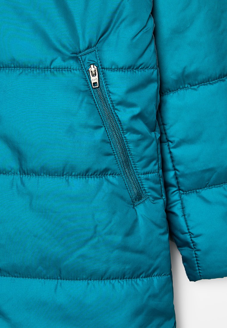 Sección de una chaqueta acolchada en color verde azulado que muestra un bolsillo con cremallera diagonal y parte de una manga con costura horizontal.