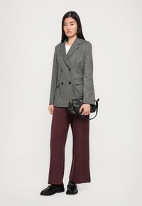 Blazer gris à double boutonnage, en tissu texturé ; associé à un pantalon large bordeaux. Sac à main matelassé noir et chaussures noires brillantes.