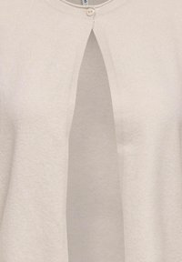 Cardigan beige clair avec un col rond et une fermeture par bouton au sommet. Présente un design fendu à l'avant et une texture douce.