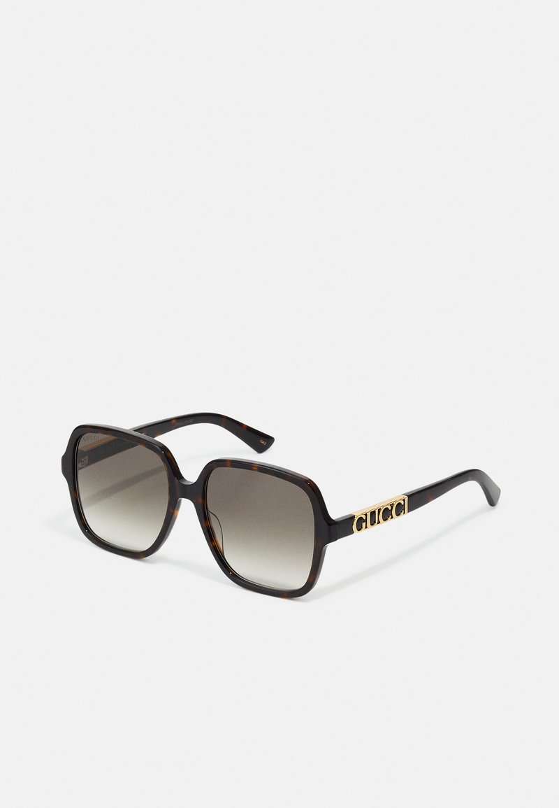 Occhiali da sole squadrati con motivo tartarugato, lenti grigie sfumate e logo "GUCCI" dorato sul lato. Realizzati in materiale plastico.