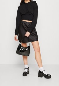 Sudadera negra corta, mini falda de cuero negra brillante y zapatos de plataforma negros de charol. También incluye un bolso negro brillante de hombro.