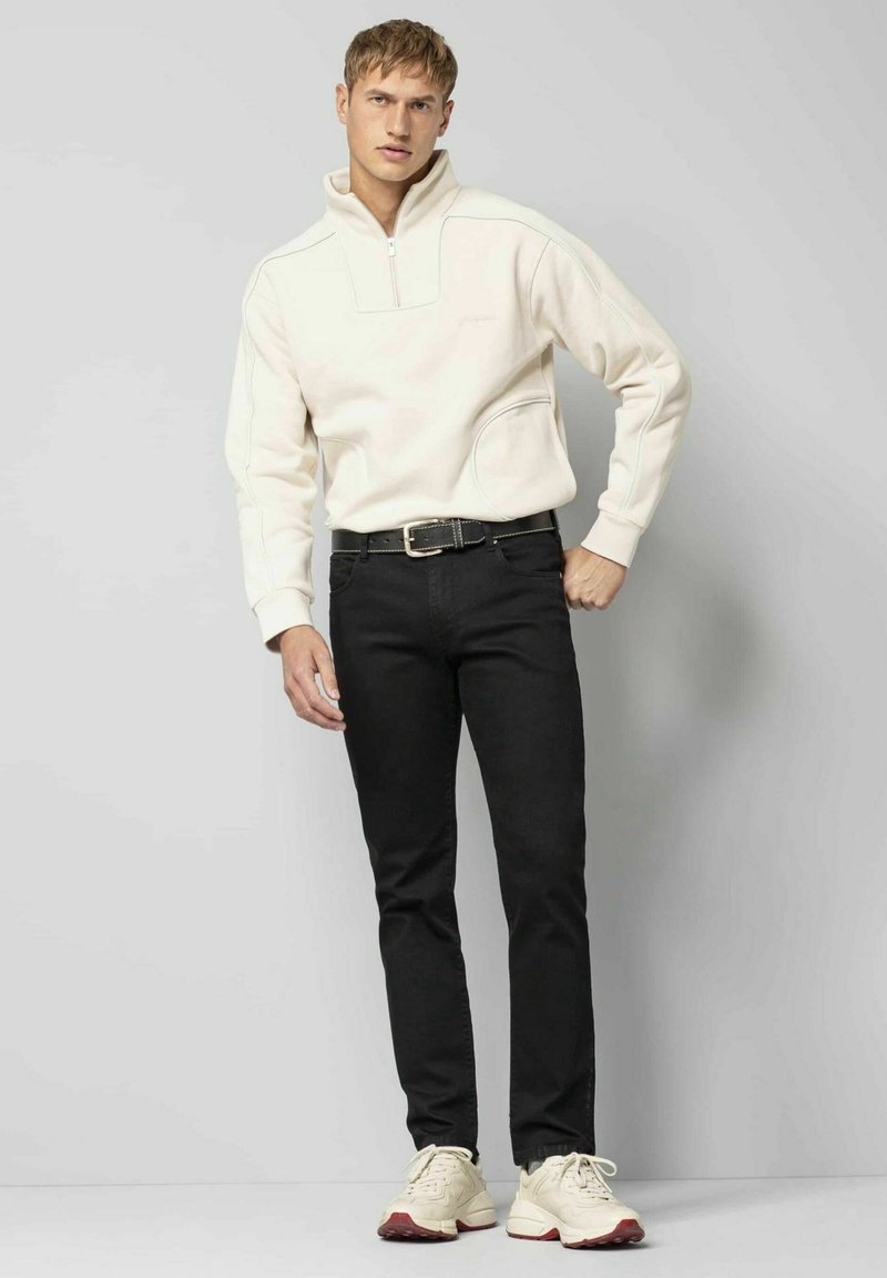 Cremiges Fleece-Half-Zip-Pullover mit einer Fronttasche, kombiniert mit schwarzen Jeans und cremigen Sneakers mit roten Akzenten. Slim-Fit-Design.