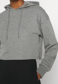 Cropped gray hoodie made of soft fabric, with a drawstring hood, long sleeves, and a relaxed fit. Paired with black bottoms.