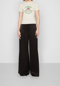 Béžové tričko s krátkým rukávem s motivem recyklace a černé široké kalhoty s hladkou texturou a volným střihem.