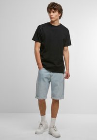 Sort bomulds t-shirt, løs pasform, parret med lyseblå denim shorts, opbøjet i kanten. Hvide sneakers og sokker i ankelhøjde fuldender outfittet.