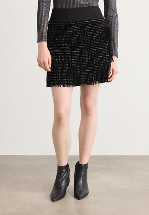 Zwarte fringe rok met metalen kraalaccenten, voorzien van een hoge taille en gelaagde textuur, gecombineerd met zwarte enkelboots.