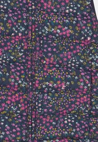 Marinblå quiltat tyg med dragkedja som har små blommönster i rosa, vitt och gult utspridda över ytan.