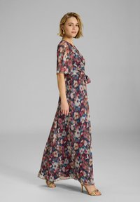 Robe maxi en tissu léger avec un imprimé floral multicolore. Présente des manches courtes, un design enveloppant, et une ceinture à la taille. Sandales dorées à brides.
