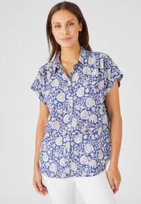 Camisa de botones de manga corta en tela azul con patrón floral blanco, que presenta un cuello clásico y un dobladillo curvado. Textura ligera y transpirable.