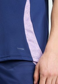 Modrý športový tielko s fialovými vzorovanými bočnými panelmi. Obsahuje logo "CLIMACOOL", hladkú textúru a priliehavý strih.