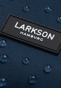 Navy fabric with a textured surface features water droplets and a black rectangular tag with white embossed text "LARKSON HAMBURG."