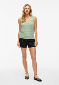 Top in maglia verde con scollatura a V, caratterizzato da un motivo testurizzato, abbinato a pantaloni corti neri e scarpe in rete. Design semplice e casual.