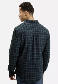 Koszula flanelowa w zielono-granatową kratę, z długimi rękawami i kołnierzykiem zapinanym na guziki. Materiał wydaje się miękki i teksturowany.