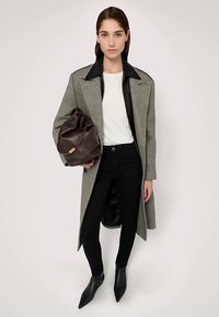 Abrigo gris de lana con cuello de cuero negro, blusa negra, vaqueros oscuros y botines negros con punta; sosteniendo un bolso de cuero marrón con un detalle dorado.