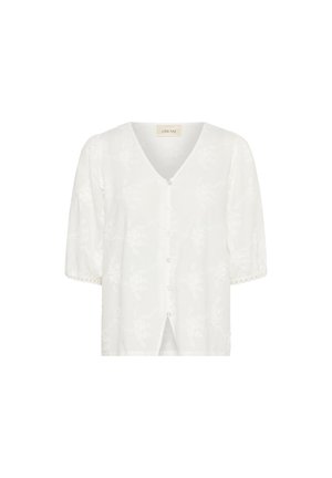 Blouse blanche avec un col en V, manches courtes bouffantes, fermeture par boutons et un motif floral gaufré sur toute la surface. Fines bordures en dentelle sur les manches.