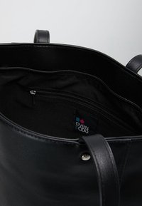 Czarna skórzana torba typu tote o gładkiej fakturze, z otwartym wierzchem i wewnętrzną kieszenią na zamek. Wyposażona w wewnętrzną metkę z logo i wytrzymałe uchwyty.