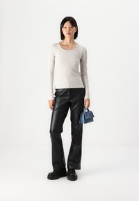 Light beige ribbed long-sleeve top paired with black high-waisted faux leather pants and a small navy blue handbag. Chunky black shoes.