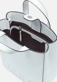 Weiße Leder-Umhängetasche mit schwarzem Innenraum, ausgestattet mit einem Magnetverschluss, innerem Reißverschlussfach und geprägtem Text auf der Außenseite.