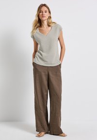 Randig V-ringad topp i vitt och grönt, matchad med lösa bruna linnebyxor. Dessa kläder kompletteras av ljusbruna sandaler.