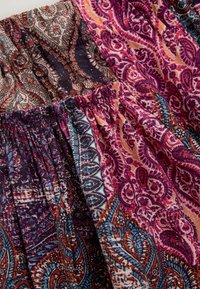 Krāsains audums ar sarežģītiem paisley un ziedu rakstiem purpursarkanā, rozā, zilā un bēša krāsā; ručota elastīga jostasvieta.