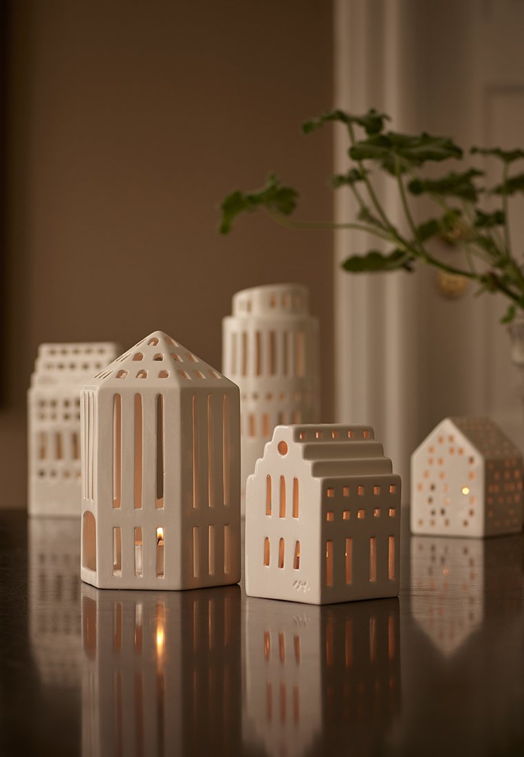 Porzellan-Kerzenhalter in Form von Gebäuden, mit ausgeschnittenen Fenstern und Dächern. Die Farben sind Weiß und sanftes Beige. Glatte, matte Oberfläche.
